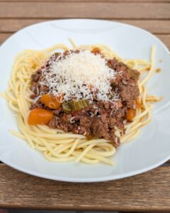 Plate of spaghetti topped with Ragù alla Bolognese and a mound of grated cheese on a wooden table