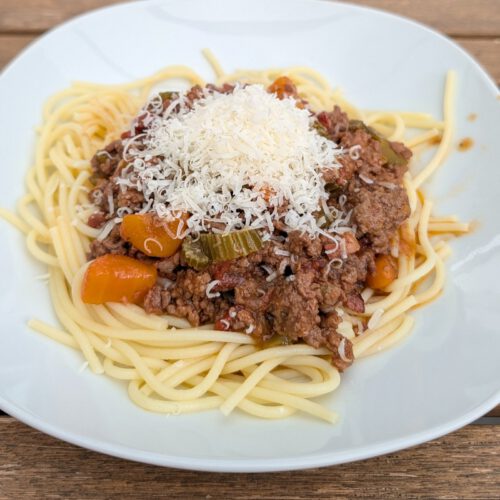 Plate of spaghetti topped with Ragù alla Bolognese and a mound of grated cheese on a wooden table