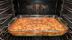 Baked moussaka in a rectangular glass baking dish in the oven with a golden-brown and dark speckled top and layers visible along the side of the dish