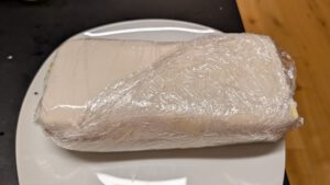 The tightly wrapped beef roll in plastic wrap chilling on a plate