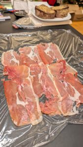 Prosciutto slices overlapping on a sheet of plastic wrap