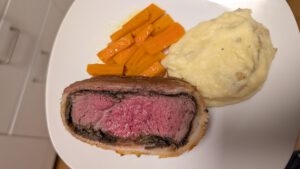 Plated slice of Beef Wellington with mashed potatoes and glazed carrots