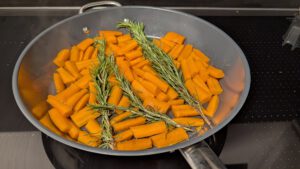 Carrot sticks with fresh rosemary sprigs in a wide pan before cooking