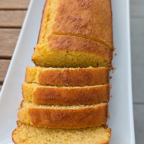Golden-brown gluten-free cornbread loaf with four cut slices lined up on a long white plate, showing a golden crust and crumbly yellow crumb