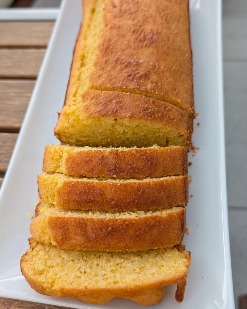 Golden-brown gluten-free cornbread loaf with four cut slices lined up on a long white plate, showing a golden crust and crumbly yellow crumb