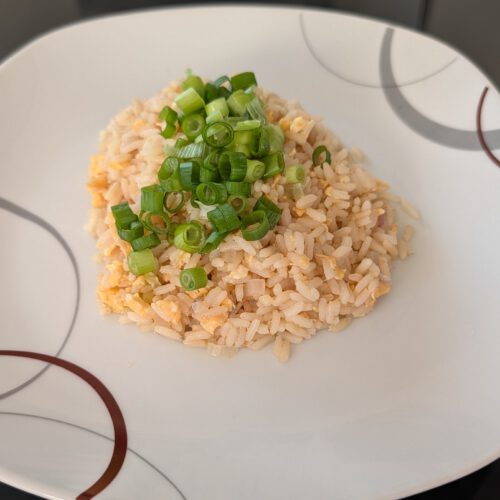 Egg fried rice with scrambled egg pieces, topped with sliced green spring onions on a white plate with gray and brown rings