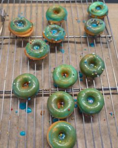 Green and blue glazed mini donuts with colourful sprinkles on a wire cooling rack lined with baking paper