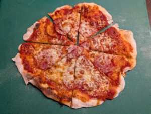 Baked pizza cut into slices on a green board