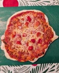 Freshly baked gluten-free pizza with browned cheese, tomato sauce and diced red bell pepper on a flour-dusted green cutting board