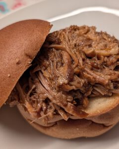 Close-up of a pulled pork burger on a bun with the top half tilted aside, on a white plate