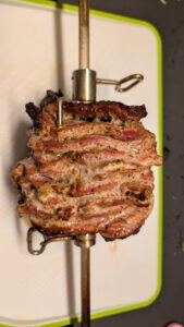 Rotisserie spit lifted out with the browned crisp layers of the meat block on a white and green cutting board