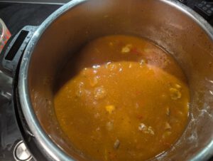 Orange-brown goulash sauce with mushrooms and bell pepper pieces bubbling in a stainless steel Instant Pot