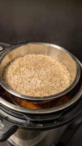 Instant Pot with a stainless steel bowl of raw buckwheat groats standing on a trivet inside the pot; the meatballs and sauce underneath are not clearly visible