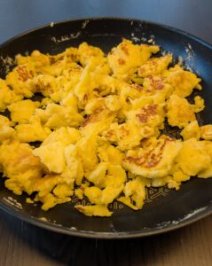 Golden torn Kaiserschmarrn pieces in a dark non-stick frying pan on a dark wooden table