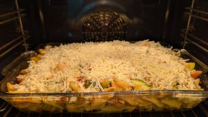 Unbaked penne casserole in a glass dish in the oven, thickly covered with shredded mozzarella