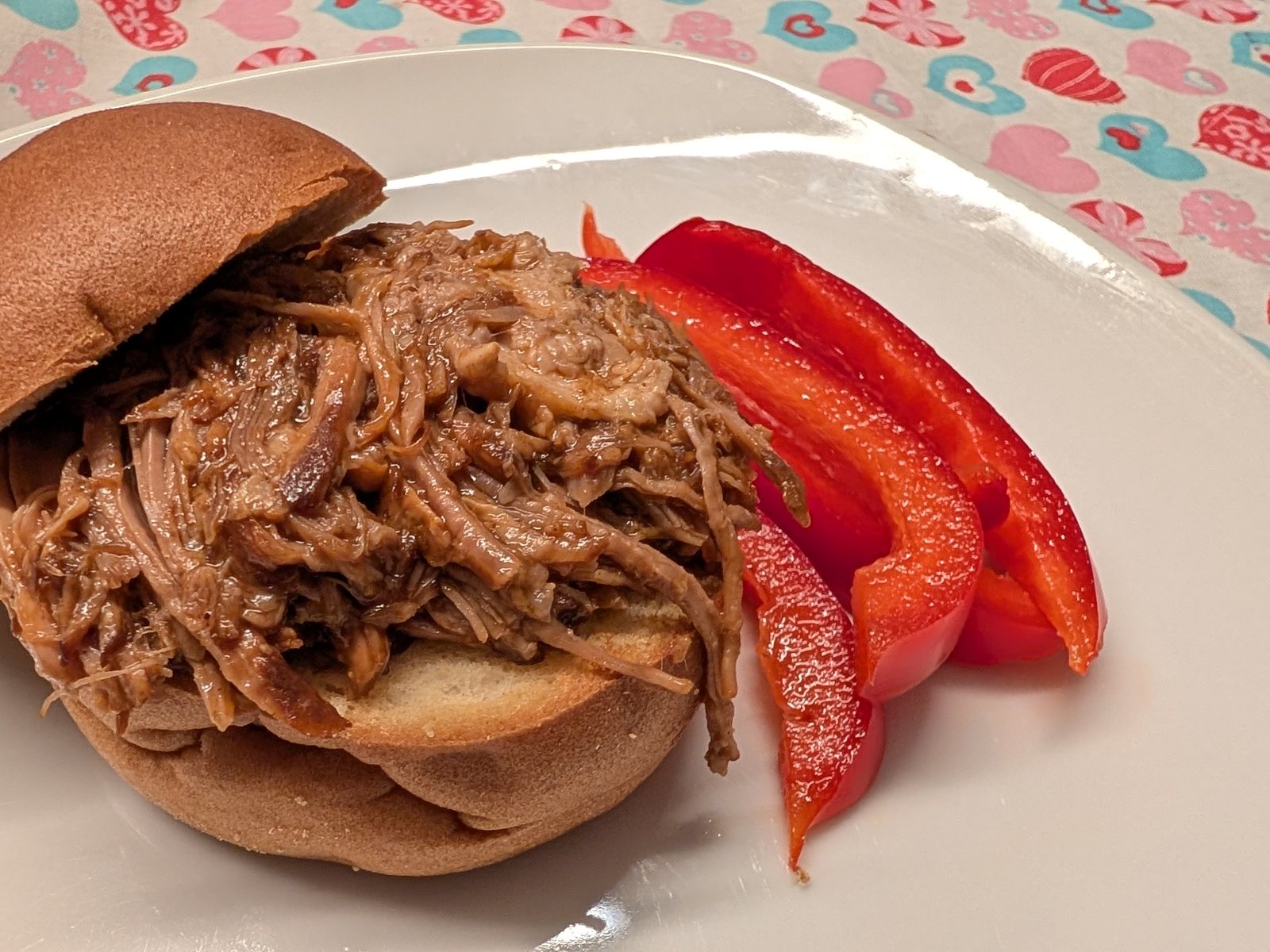 Gluten-free pulled pork burger on a white plate with red pepper strips