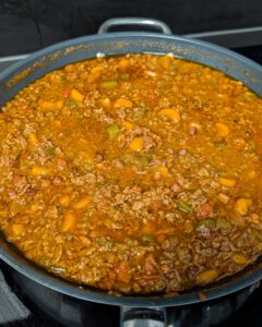 Ragù alla Bolognese simmering in a wide pan with ground beef, pancetta, carrot and celery pieces