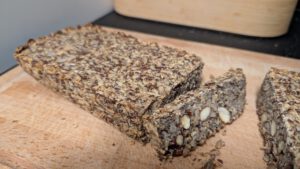 Baked flat-topped seed bread loaf with one slice cut off, whole almonds and seeds visible in the dense crumb