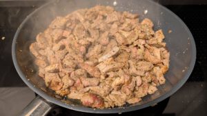 Cooked pork pieces in a grey frying pan with steam rising