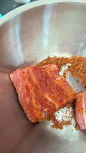 Raw pork rib sections coated in a red-brown dry rub in a stainless steel bowl