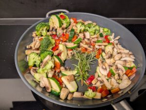 Broccoli, mushrooms, zucchini and red bell pepper arranged around the edge of a pan with rosemary sprigs in the middle