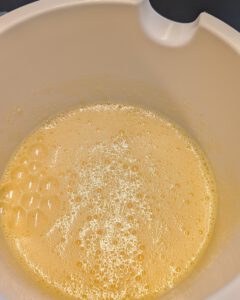 Pale yellow whisked egg and sugar mixture with fine bubbles in a white mixing bowl